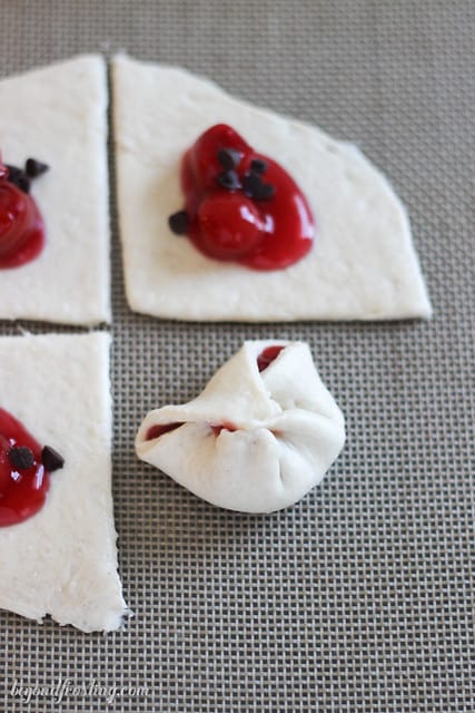 Overhead view of cherry pie filling and mini chocolate chips on squares of dough with one folded closed