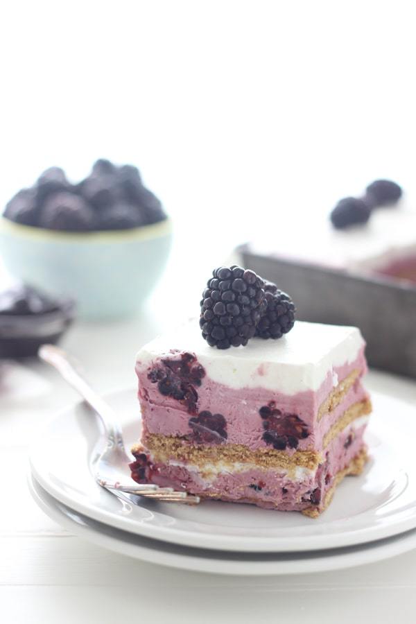 A white plate with a slice of blackberry ice cream cake is topped with 3 fresh blackberries