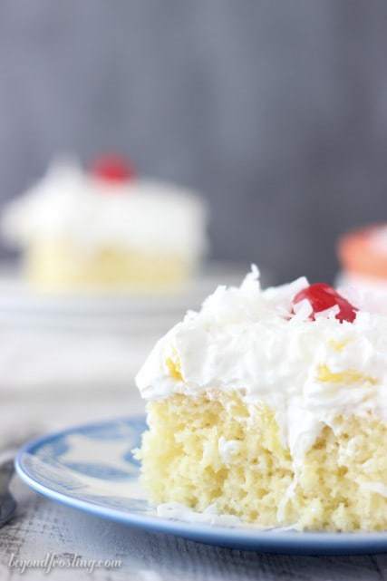 A Piece of Pina Colada Poke Cake Topped with Coconut Flakes and a Cherry