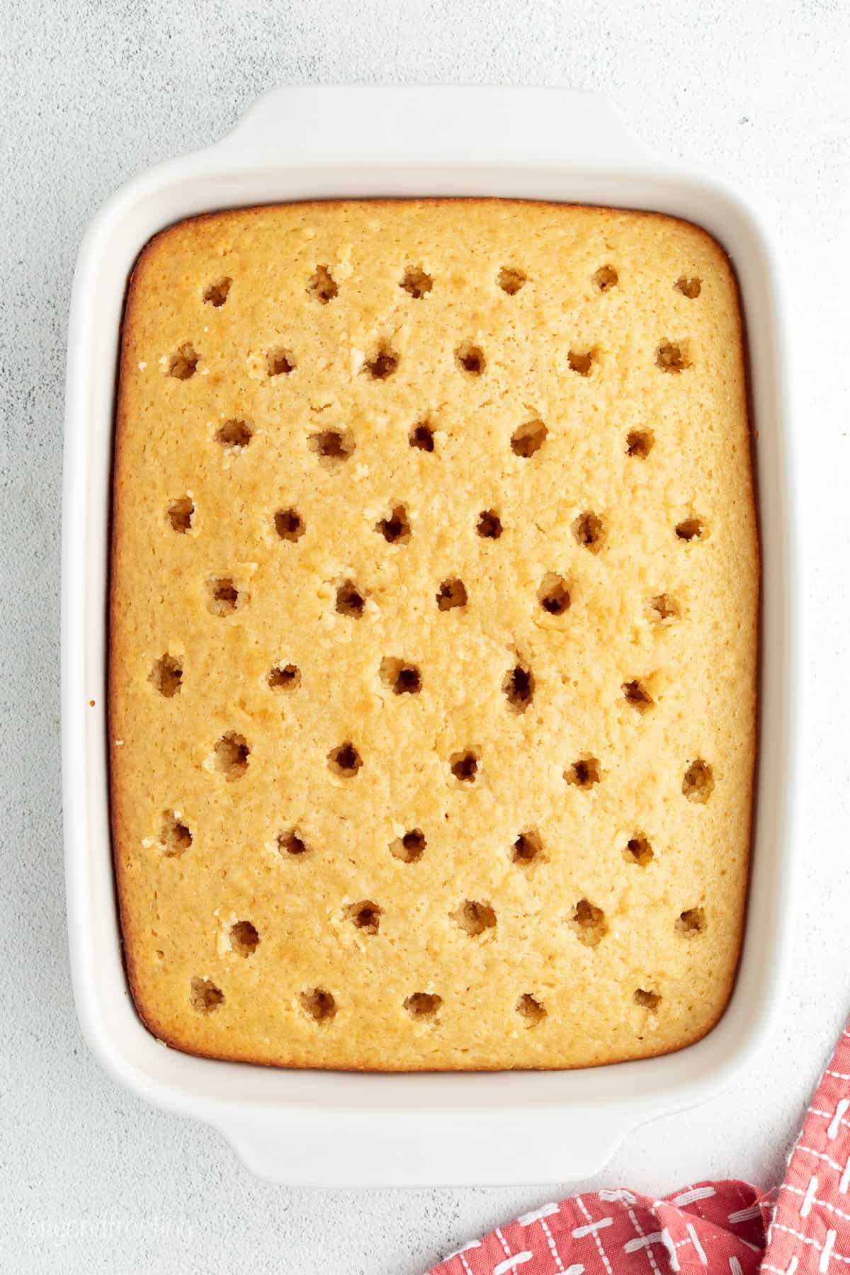 Overhead view of a vanilla cake with holed poked all over the top.