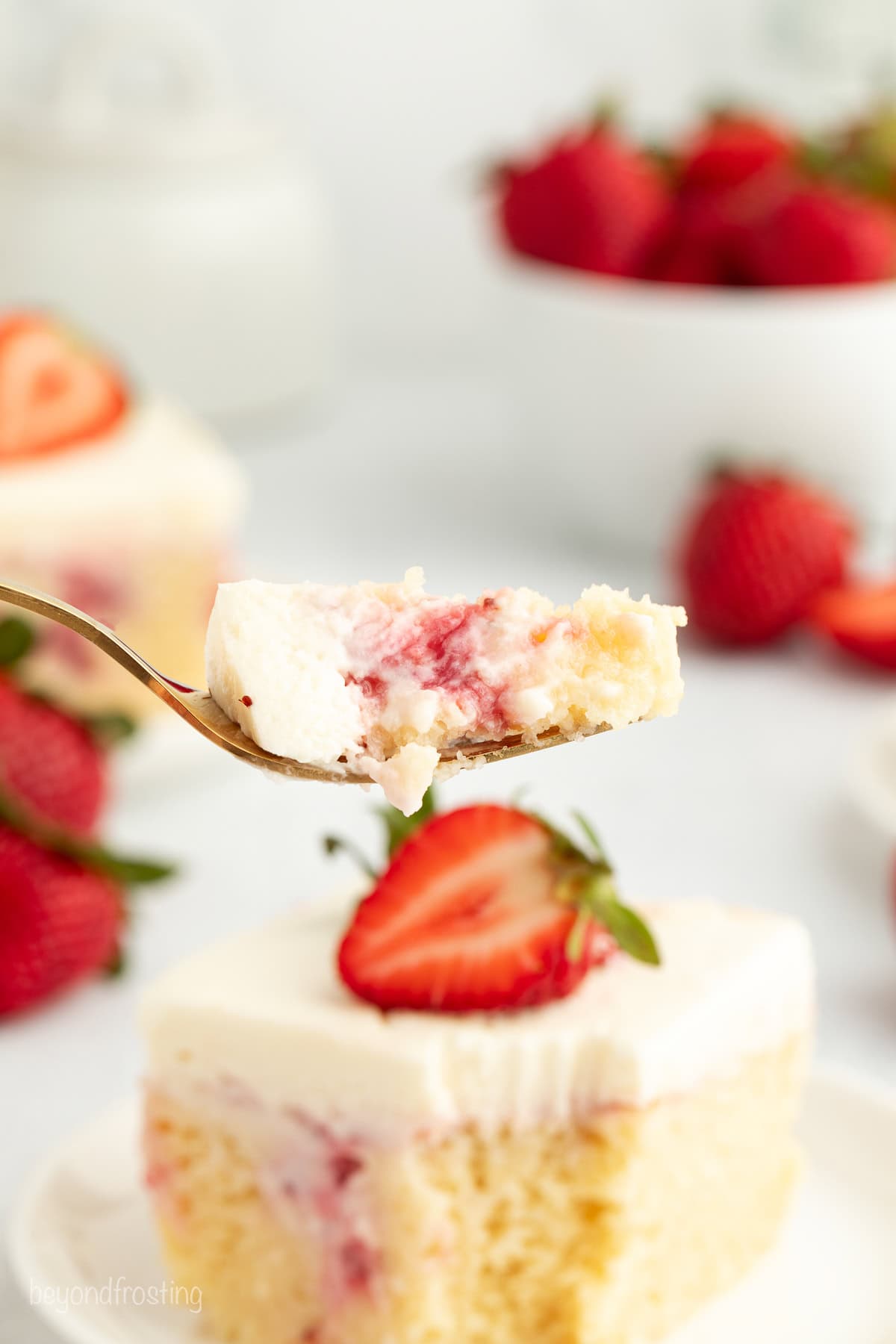 Close up of a forkful of strawberry cheesecake poke cake held up with a slice of cake in the background.