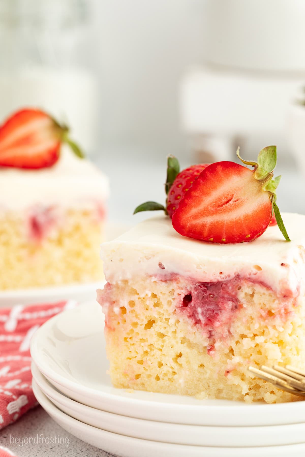 A slice of strawberry cheesecake poke cake garnished with fresh strawberries on a white plate.
