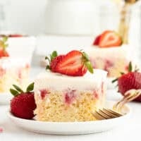A slice of strawberry cheesecake poke cake garnished with fresh strawberries on a white plate next to a fork.