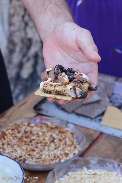 A hand holding an open-faced S'more with a variety of toppings