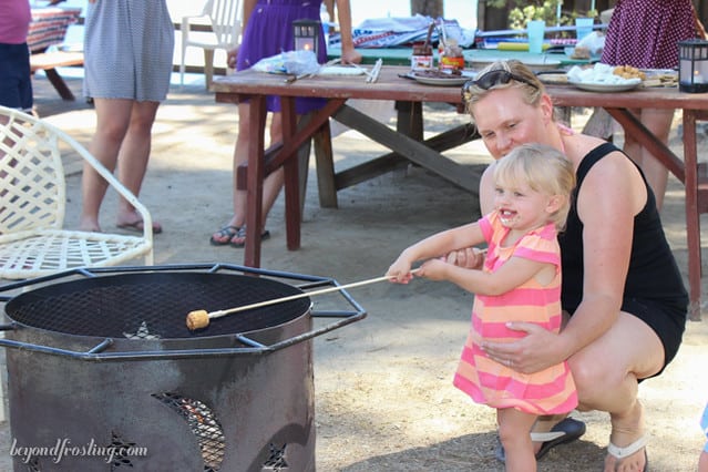 A mom helping a little girl toast a marshmallow over the fire