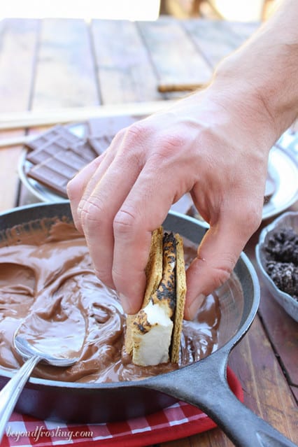 A s'more being dipped into melted chocolate in a skillet