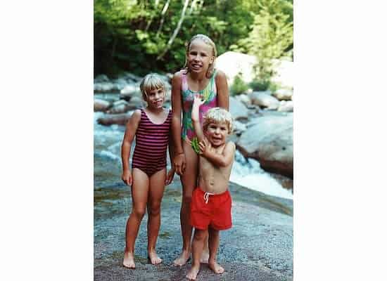 Three kids in bathing suits in front of a rocky river