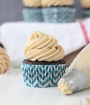 A Biscoff cheesecake cupcake topped with cream cheese frosting next to a piping tip.