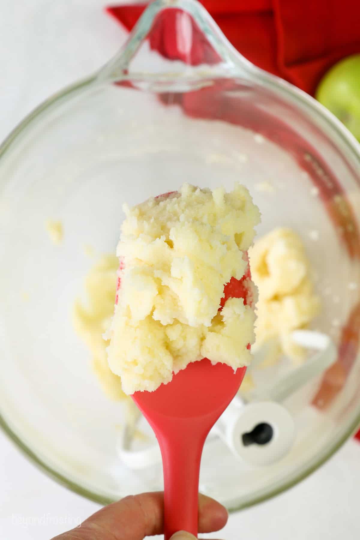 Overhead view of creamed butter on a red rubber spatula, held over a mixing bowl.