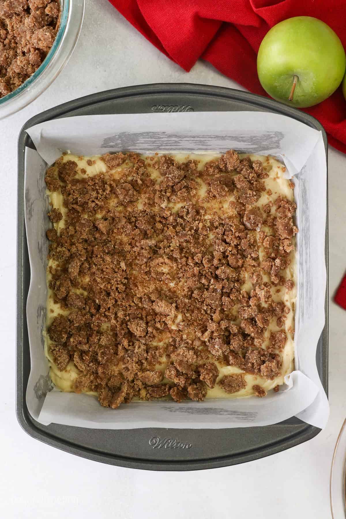 Streusel layered over coffee cake batter in a lined square baking pan.