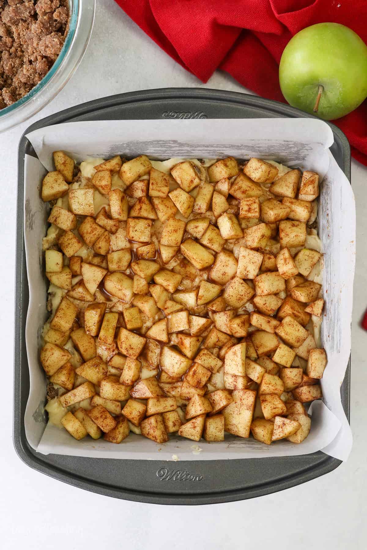 Apples added over top of the apple coffee cake layers in a lined square pan.