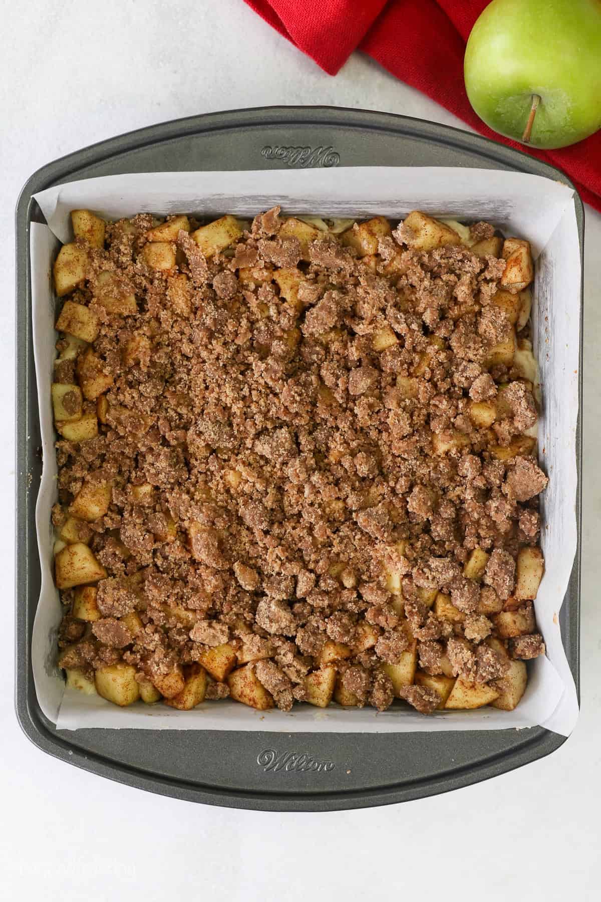 A final streusel topping added to the rest of the apple coffee cake layers in a lined square pan.