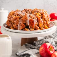 Glazed apple monkey bread on a cake stand next to whole red apples.