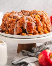 Glazed apple monkey bread on a cake stand next to whole red apples.