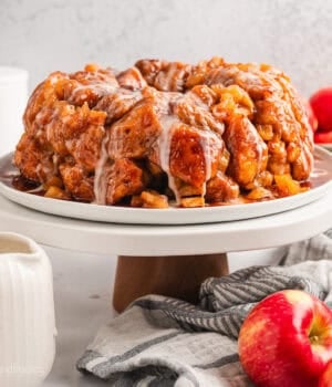 Glazed apple monkey bread on a cake stand next to whole red apples.