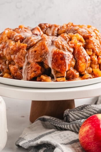 Glazed apple monkey bread on a cake stand next to whole red apples.