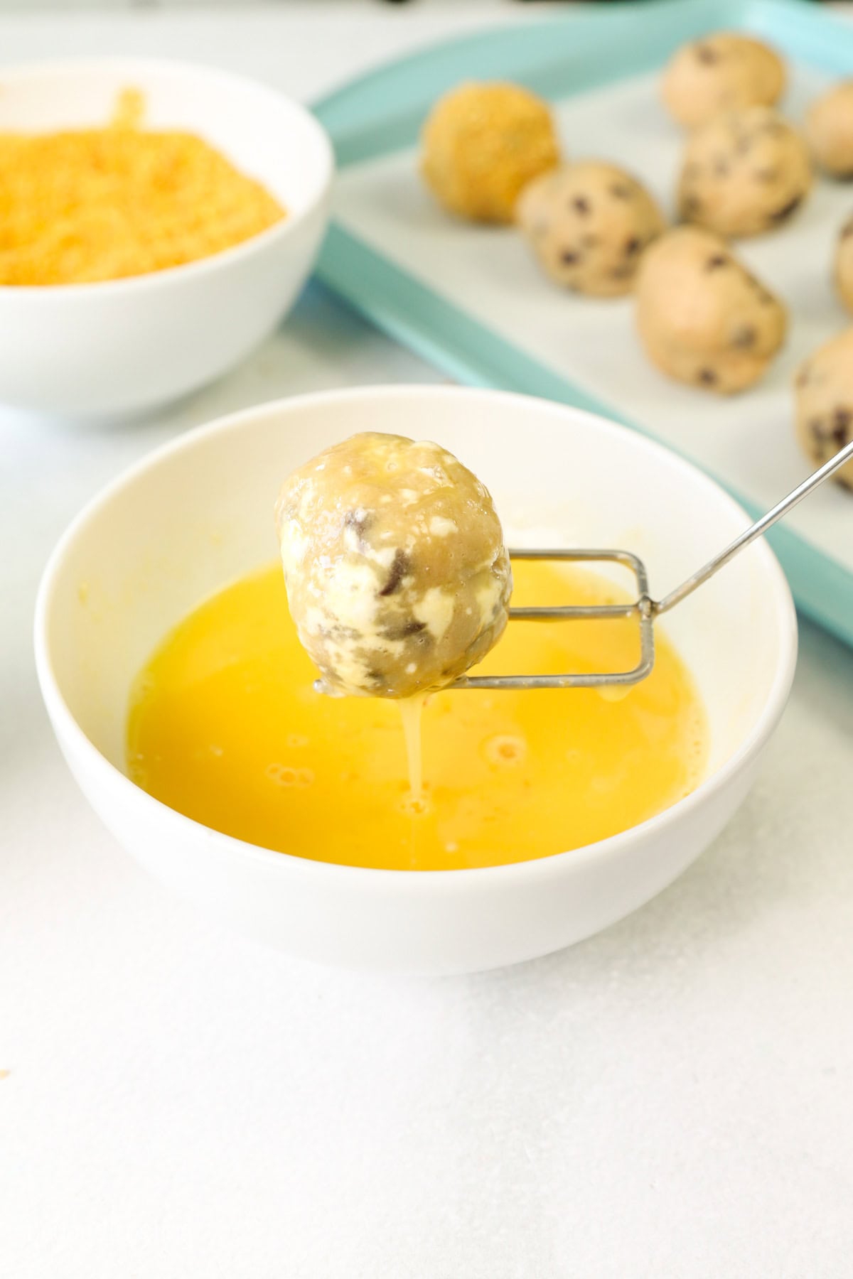 A cookie dough ball being lifted from a small bowl of egg wash.