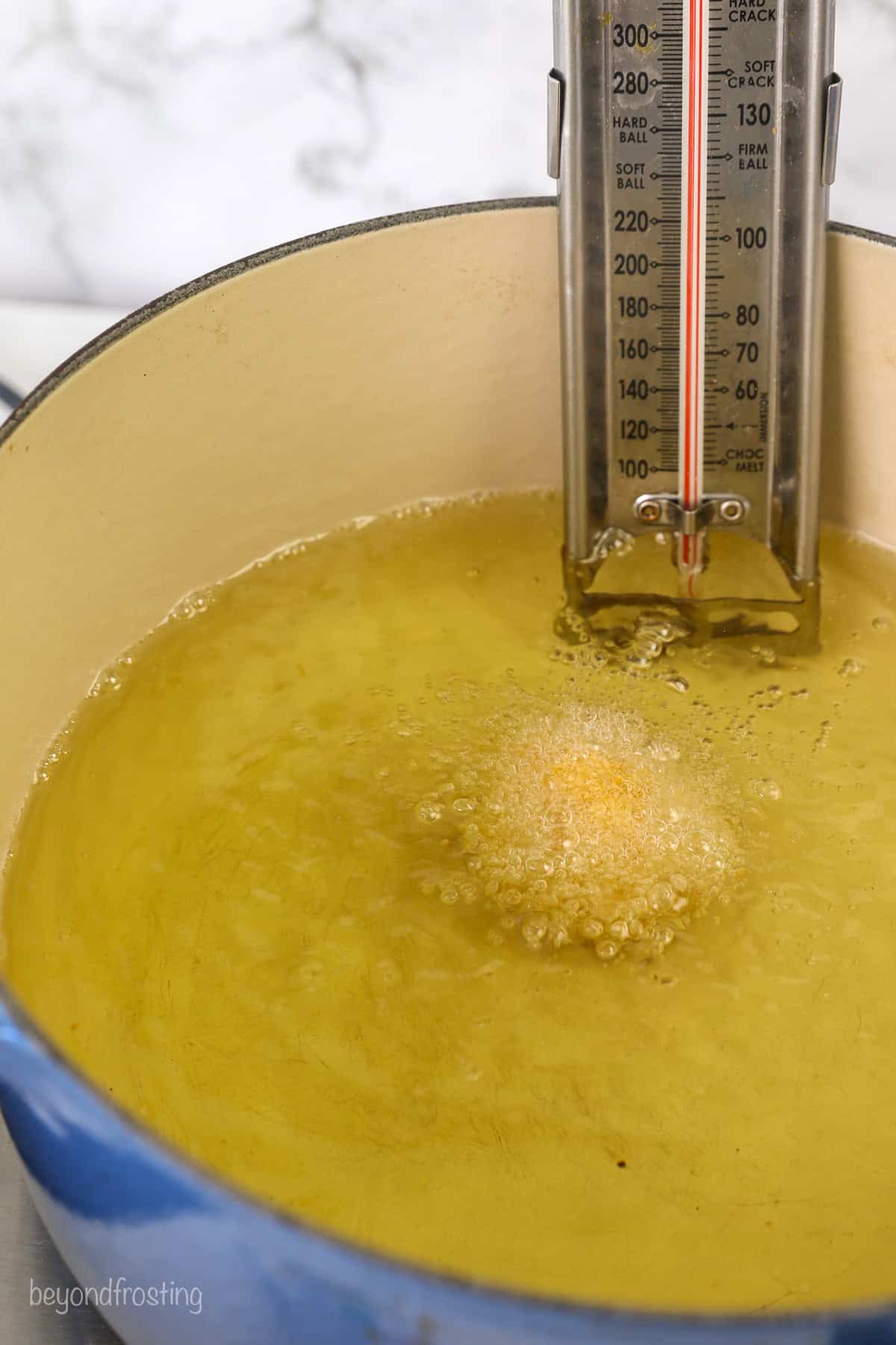 A cookie dough ball deep frying in a pot of hot oil fitted with a candy thermometer.