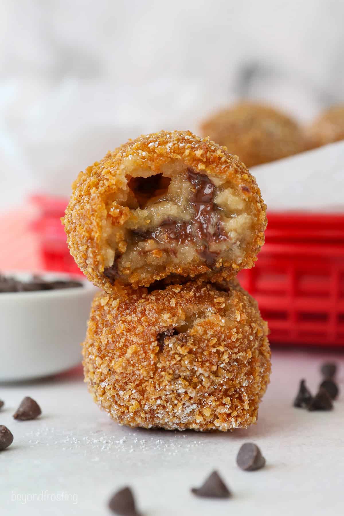 Two deep fried cookie dough balls stacked on top of one another, with a bite missing from the top ball.