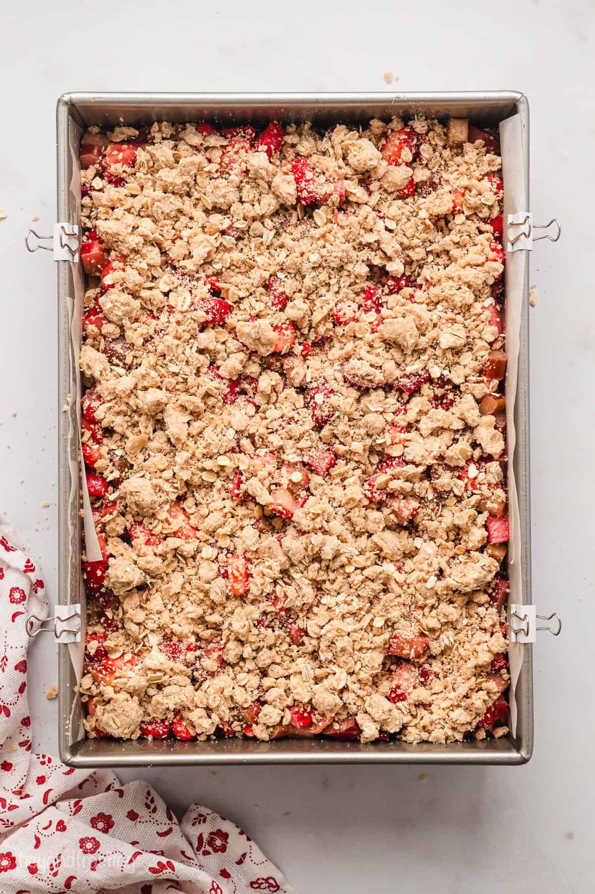 Assembled strawberry rhubarb crumb bars in a lined baking pan.