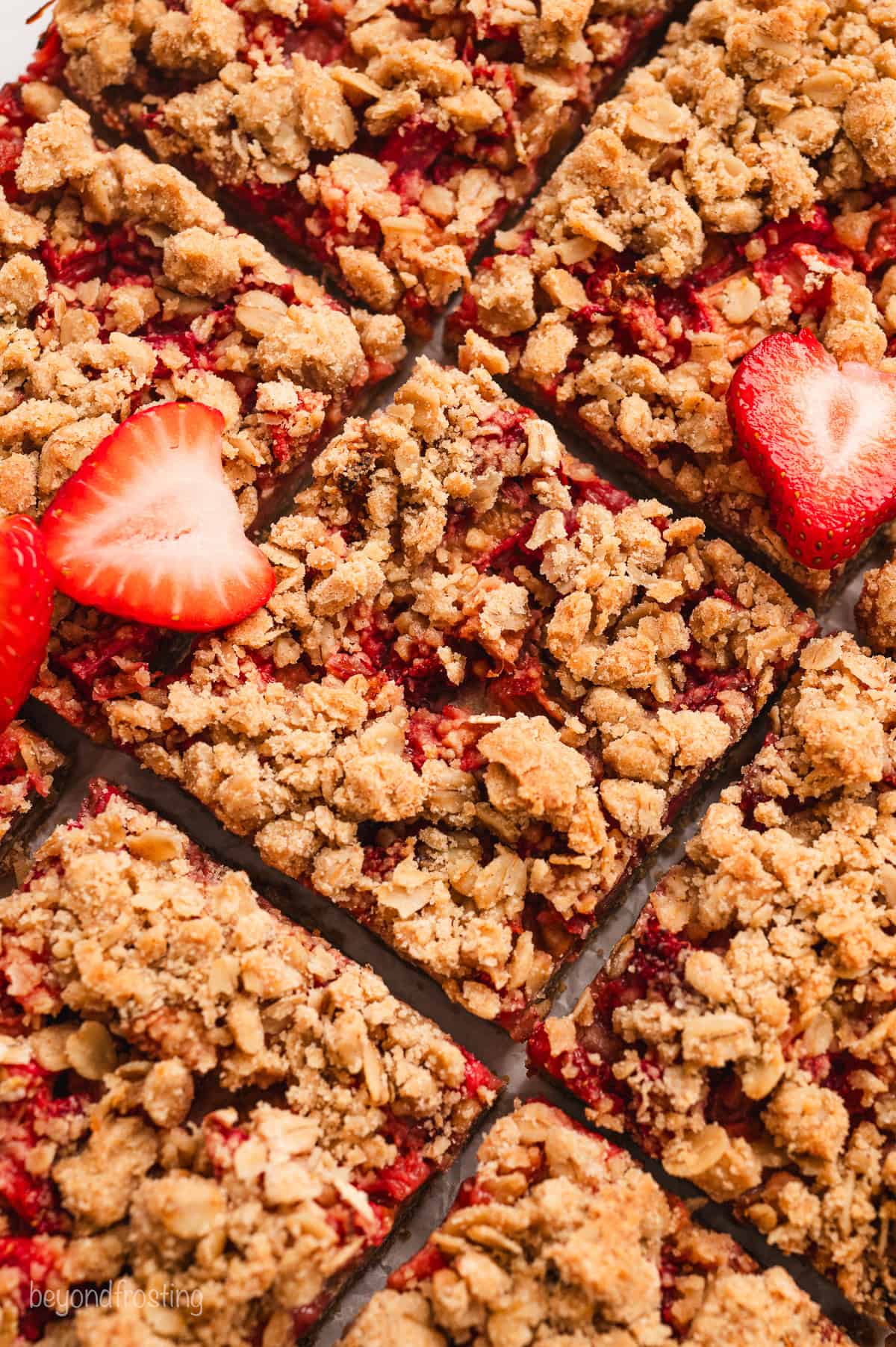 Overhead close up view of freshly cut strawberry rhubarb bars garnished with two fresh strawberry slices.