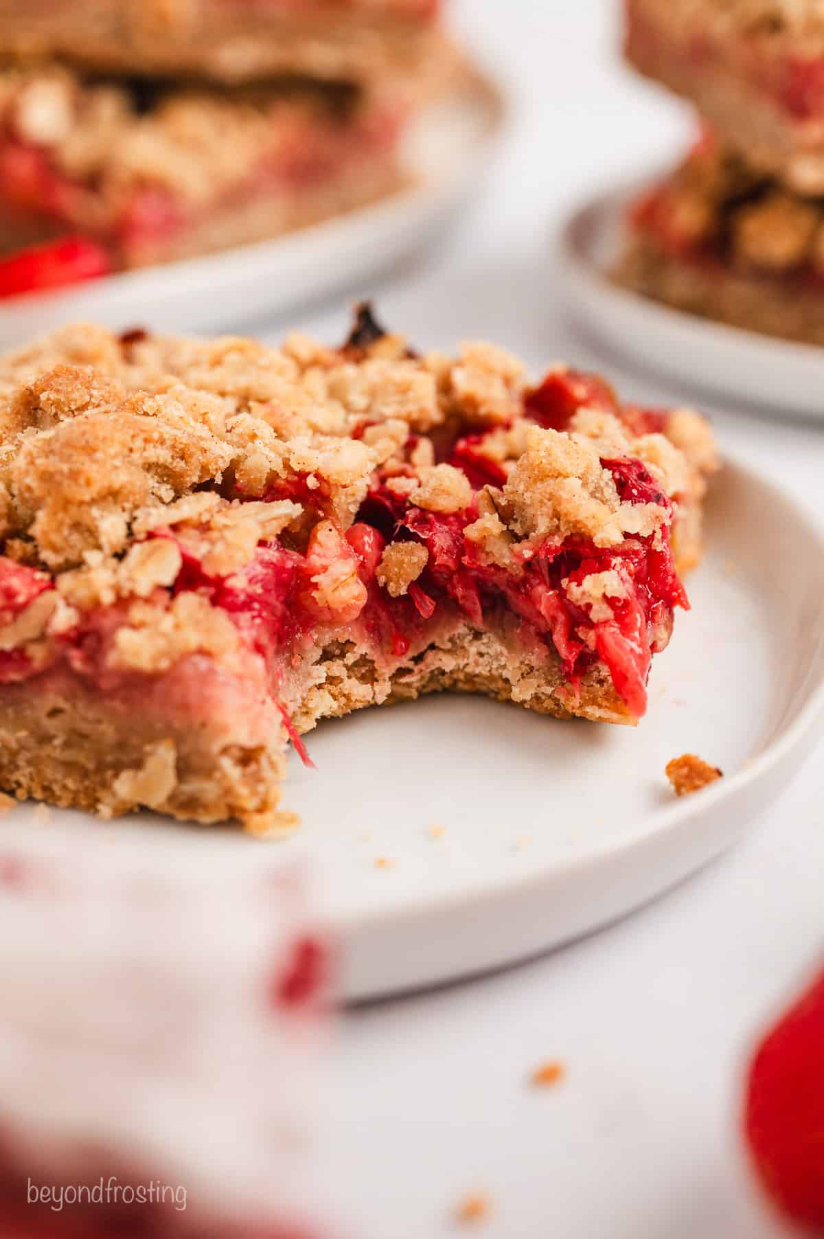 A strawberry rhubarb bar with a bite missing on a white plate.