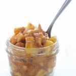 A small glass mason jar filled with apple pie filling and a silver spoon