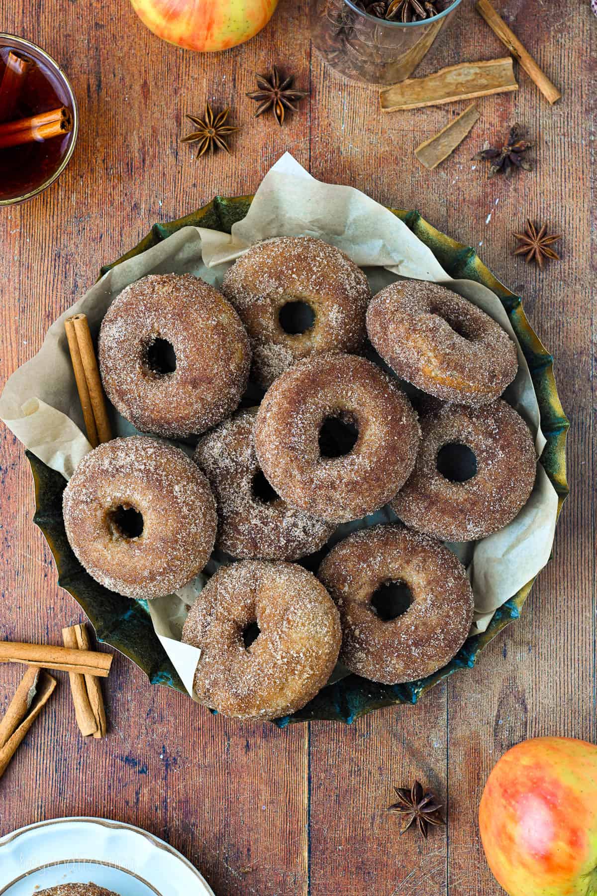 Overhead view of assorted baked apple cider donuts stacked on a parchment-lined platter on a wooden countertop.