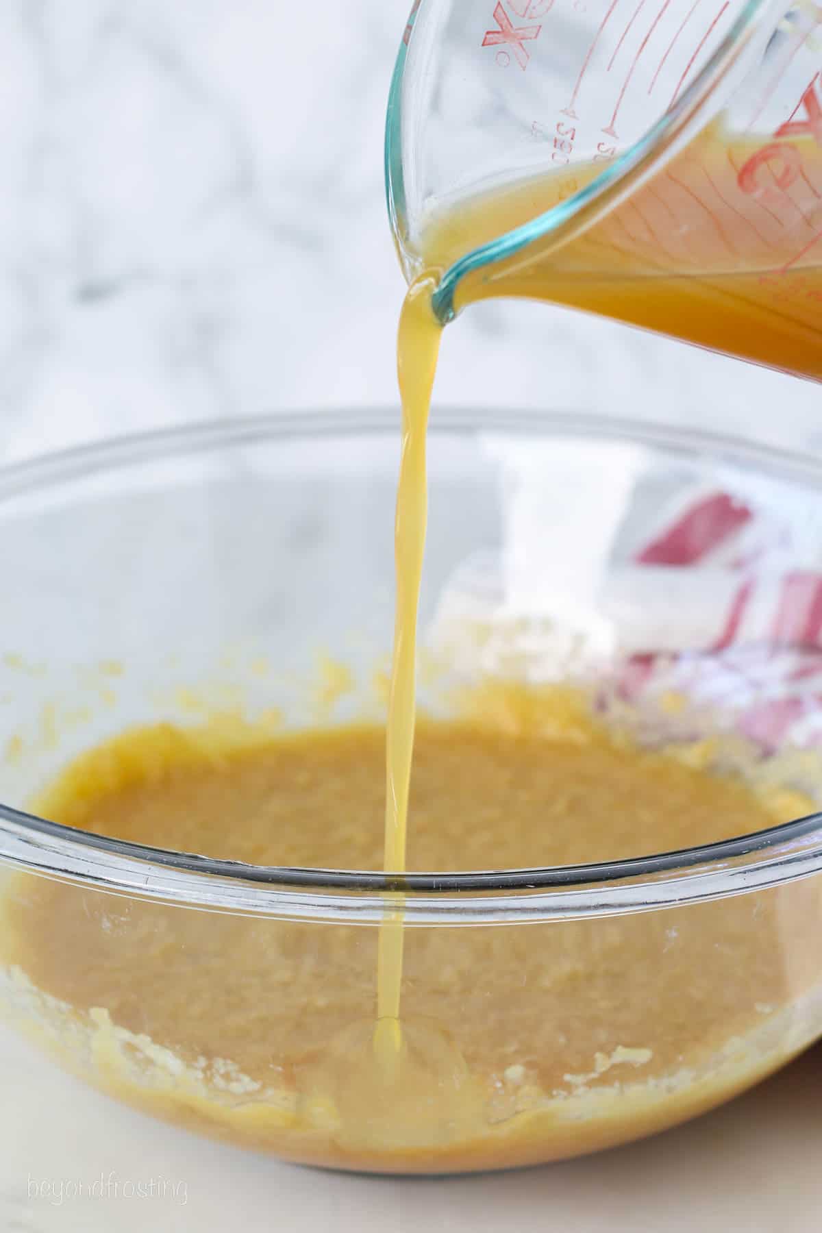 Boiled cider is poured into a glass mixing bowl with wet batter ingredients.