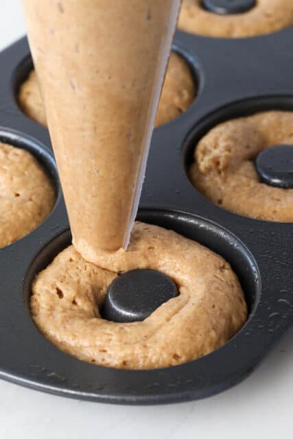 A piping bag is used to pipe apple cider donut batter into a donut pan.