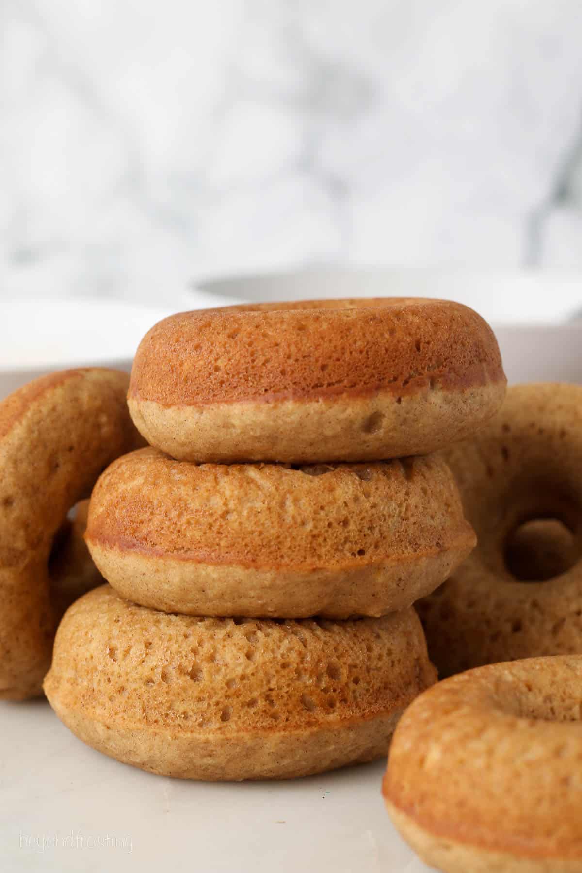 Three apple cider donuts stacked on a countertop, next to more donuts.