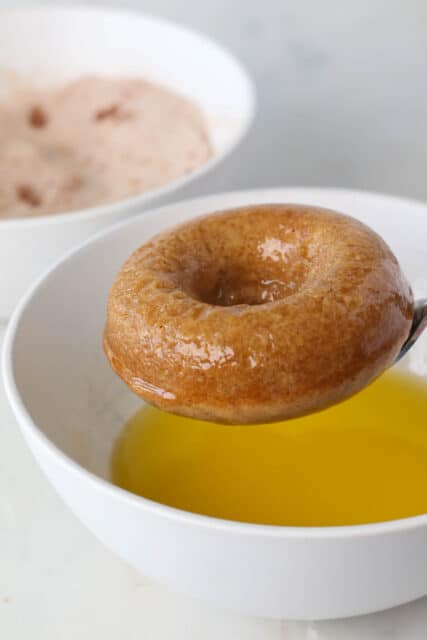 A dipped apple cider donut held over a bowl of melted butter.