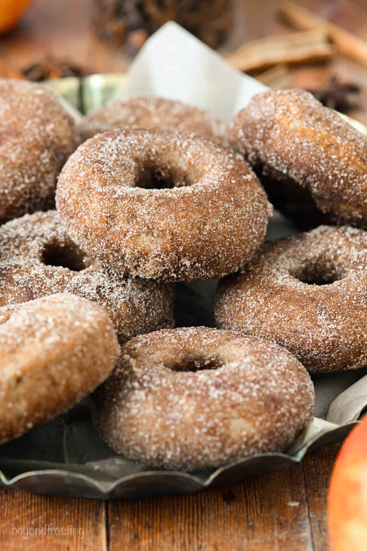 Assorted baked apple cider donuts stacked on a parchment-lined platter.