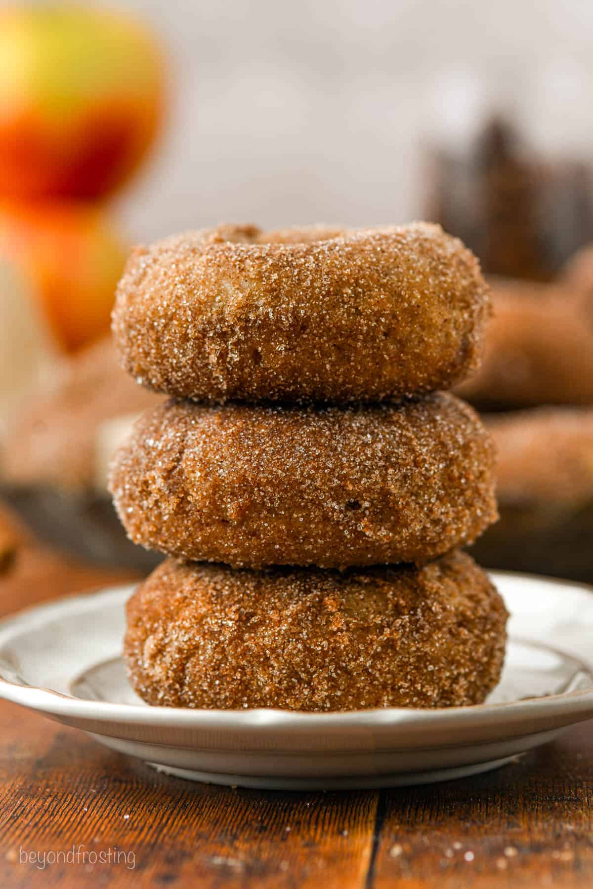 Three apple cider donuts stacked on top of one another on a white plate.