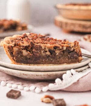 A slice of bourbon chocolate pecan pie on a plate with the rest of the pie in the background.