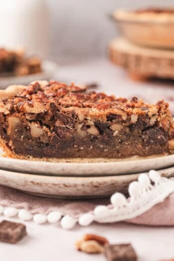 A slice of bourbon chocolate pecan pie on a plate with the rest of the pie in the background.