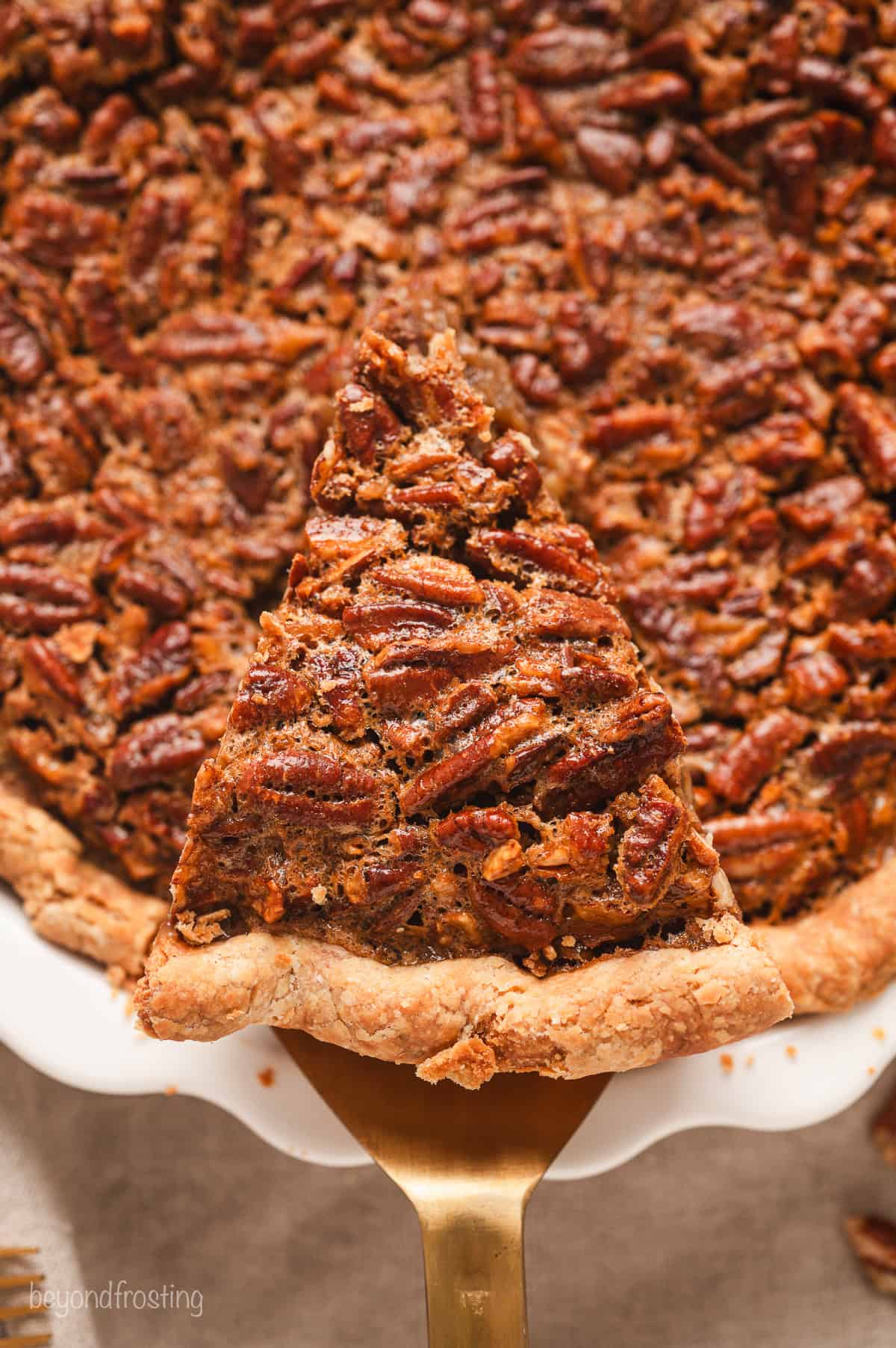 Close up overhead view of a cake server lifting a slice of pecan pie from the rest of the pie.