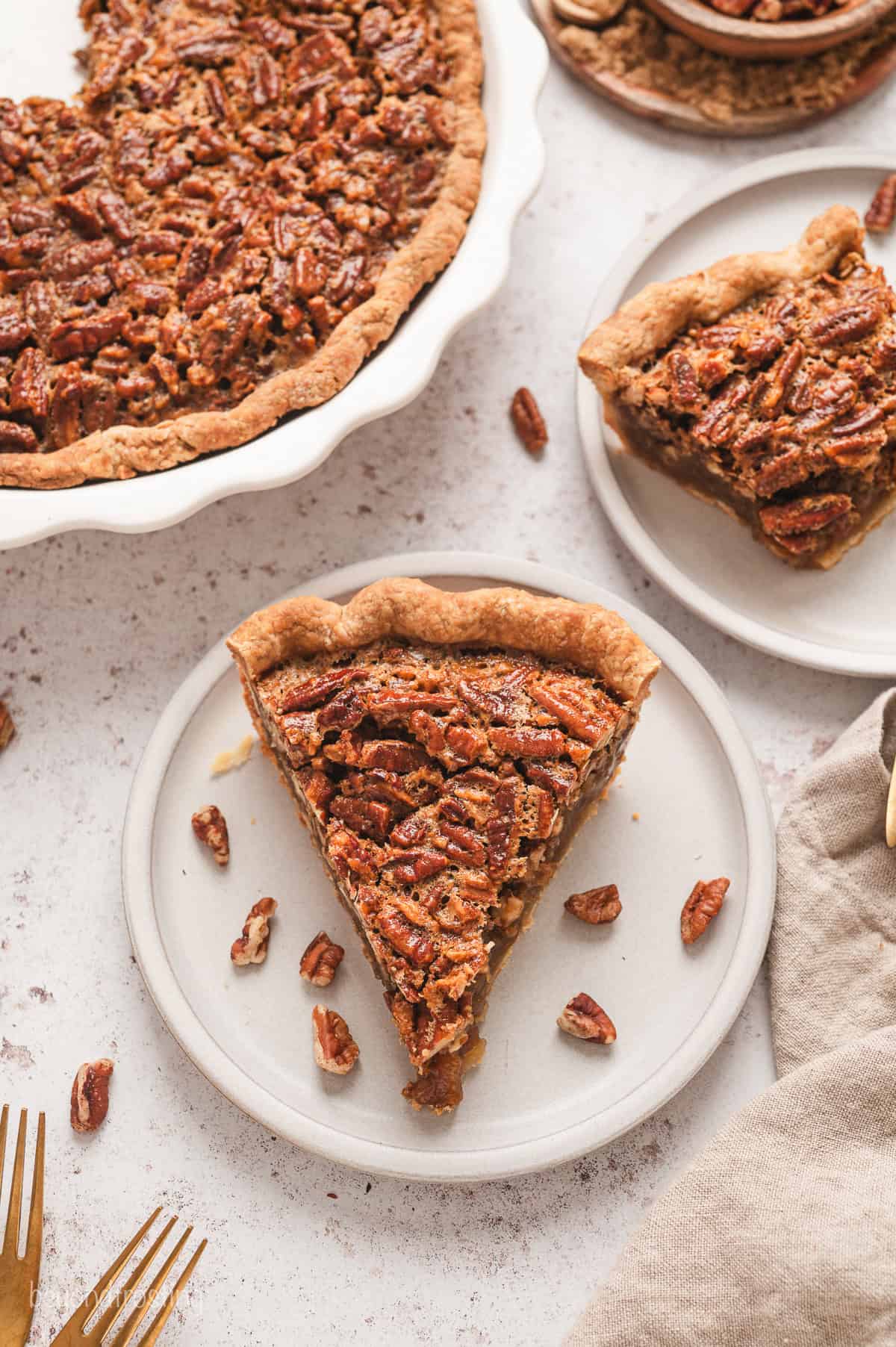 Overhead view of two pecan pie slices on plates next to the rest of the pie.