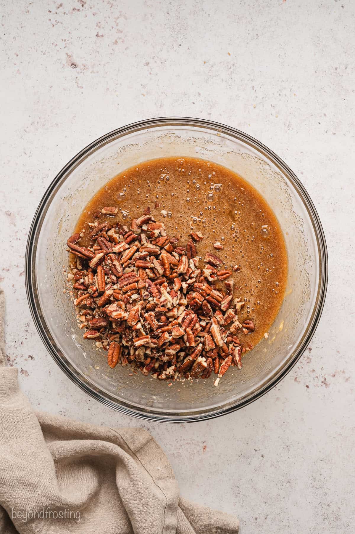 Pecans added to pie filling in a glass bowl.