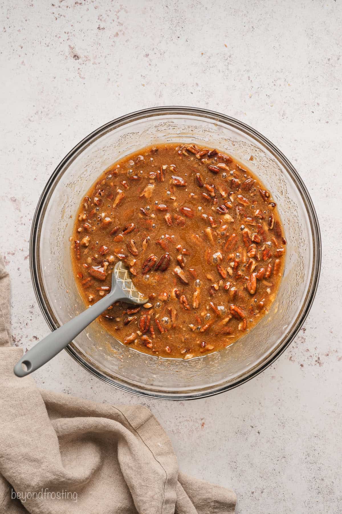 Pecan pie filling in a glass bowl with a spatula for stirring.