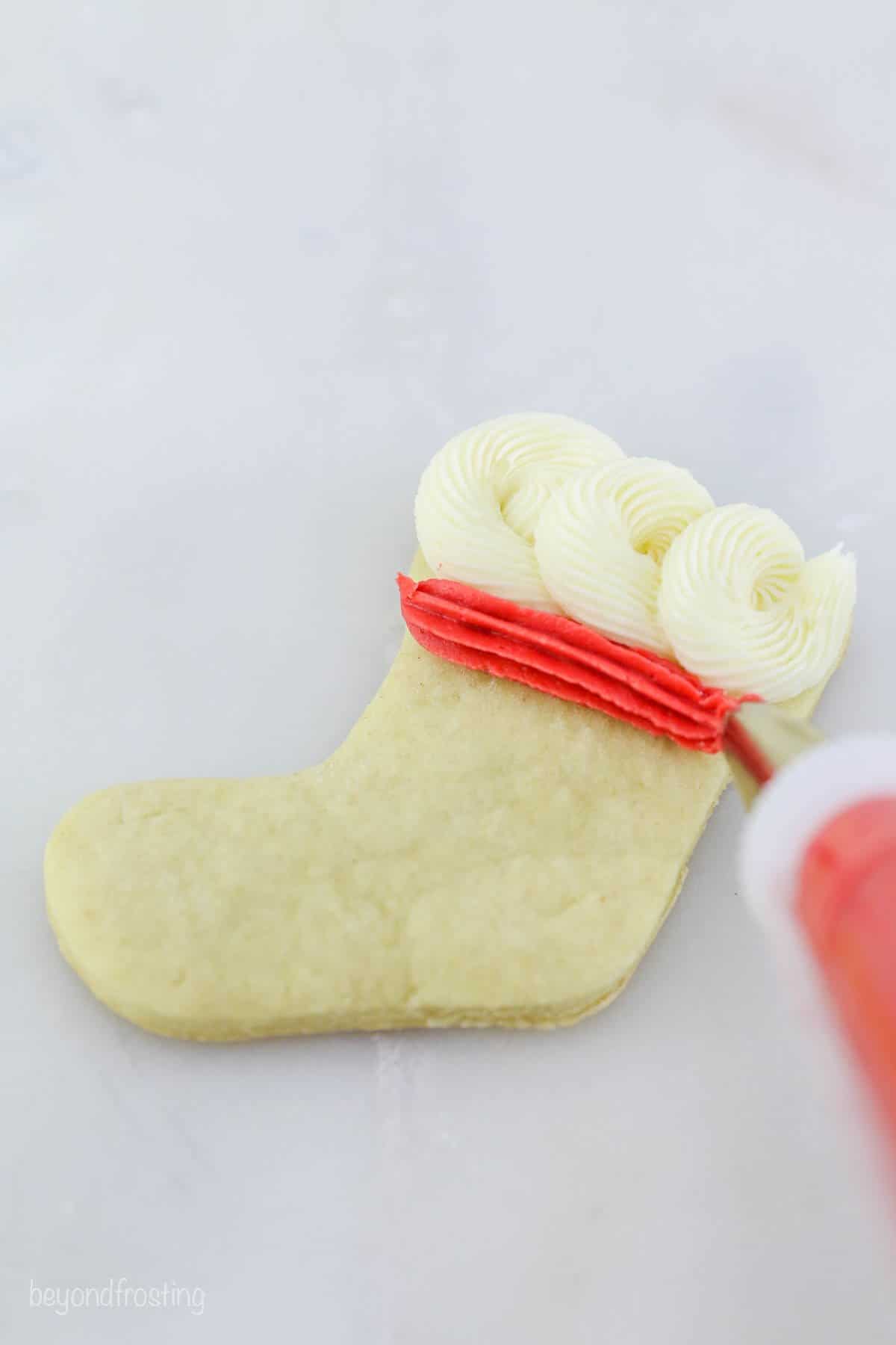 White frosting rosettes and a strip of red frosting on a stocking shaped sugar cookie