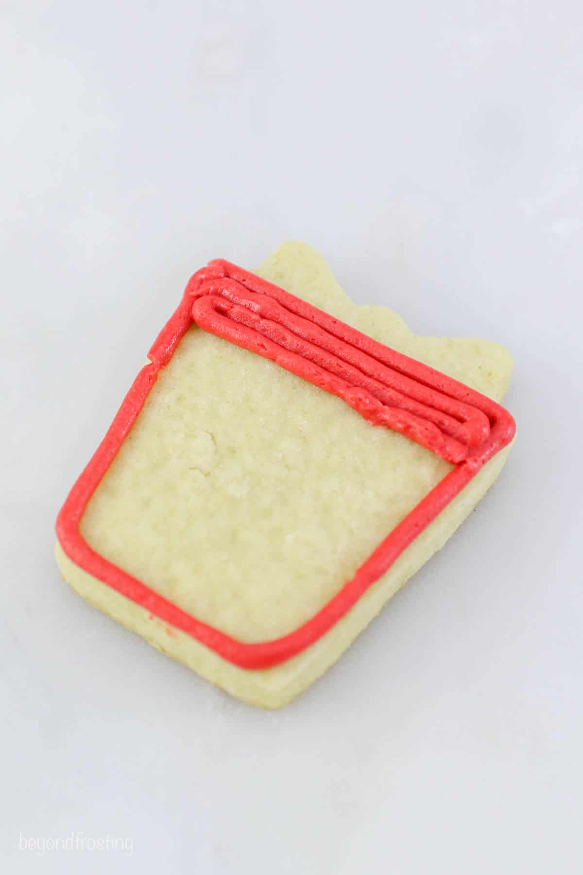 Red frosting filling in a square on a sugar cookie