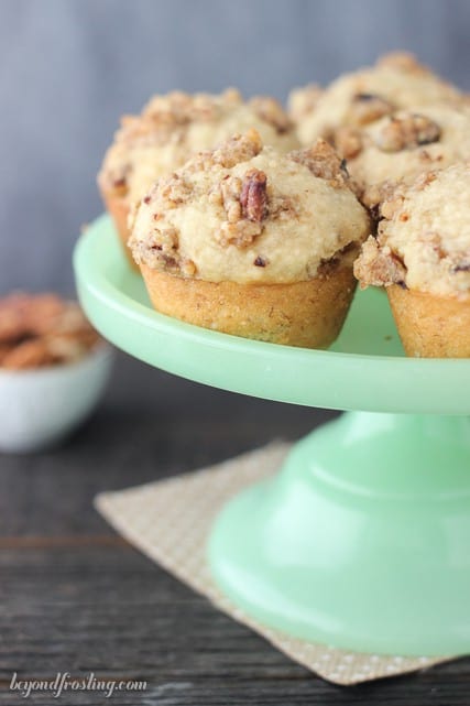 Bakery-style breakfast muffins with maple syrup and a maple pecan streusel arranged on a plastic cake stand