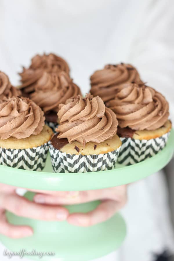 A light teal cake stand filled with cupcakes frosted with chocolate frosting