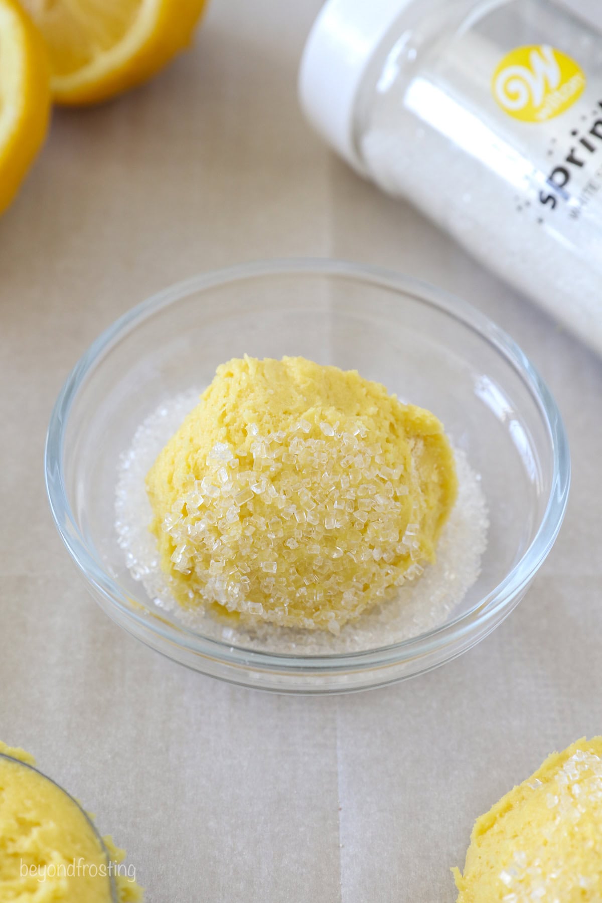 A ball of lemon cookie dough resting in a small glass bowl of sanding sugar.