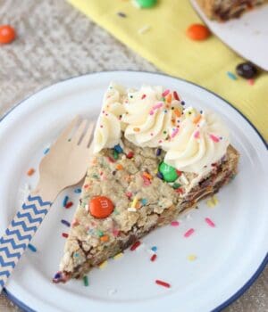 A slice of Funfetti filled Cake Batter Monster Cookie Cake topped with vanilla buttercream and sprinkles on a plate.