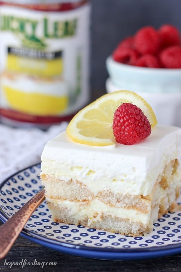 A slice of lemon icebox cake topped with whipped cream, a lemon slice, and a raspberry on a plate.