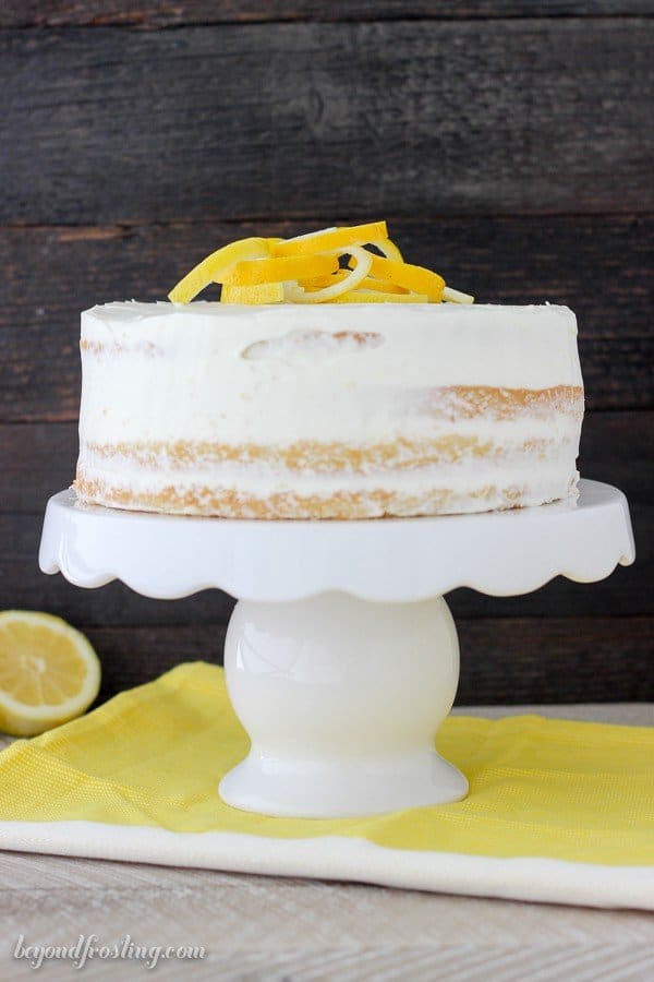 Lemon Olive Oil Cake with lemons on top sitting on a white cake stand