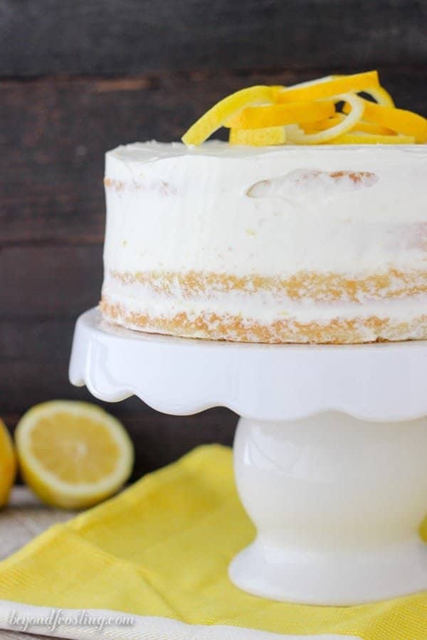 Lemon Olive Oil Cake is covered with a lemon cream cheese whipped cream on a cake stand