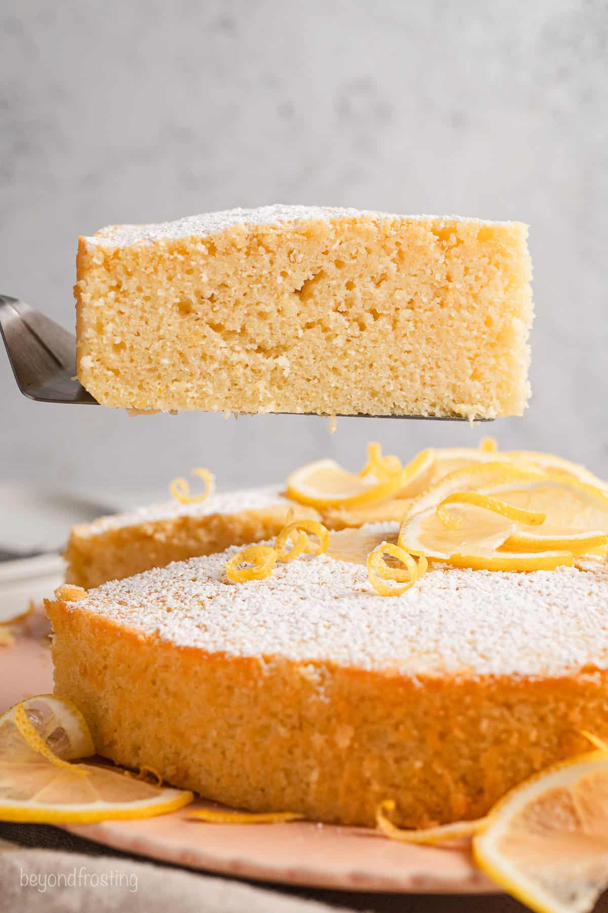 Side view of a slice of lemon olive oil cake lifted from the rest of the cake with a cake server.